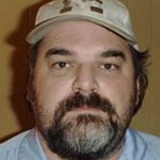 Dark-haired man with a round face and dark facial hair, wearing a baseball cap